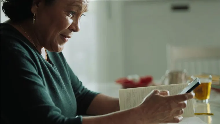 Mulher aprende sobre dólar digital no celular, à mesa da cozinha.